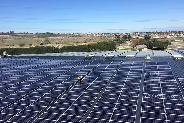 A vast warehouse roof array with a technician mid-install