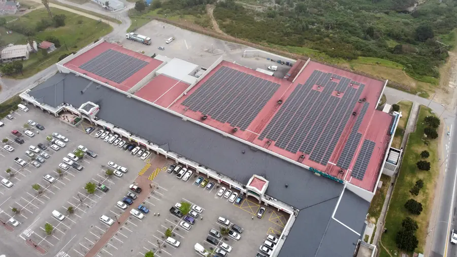 A shopping centre with arrays on its red roofs above a full car park