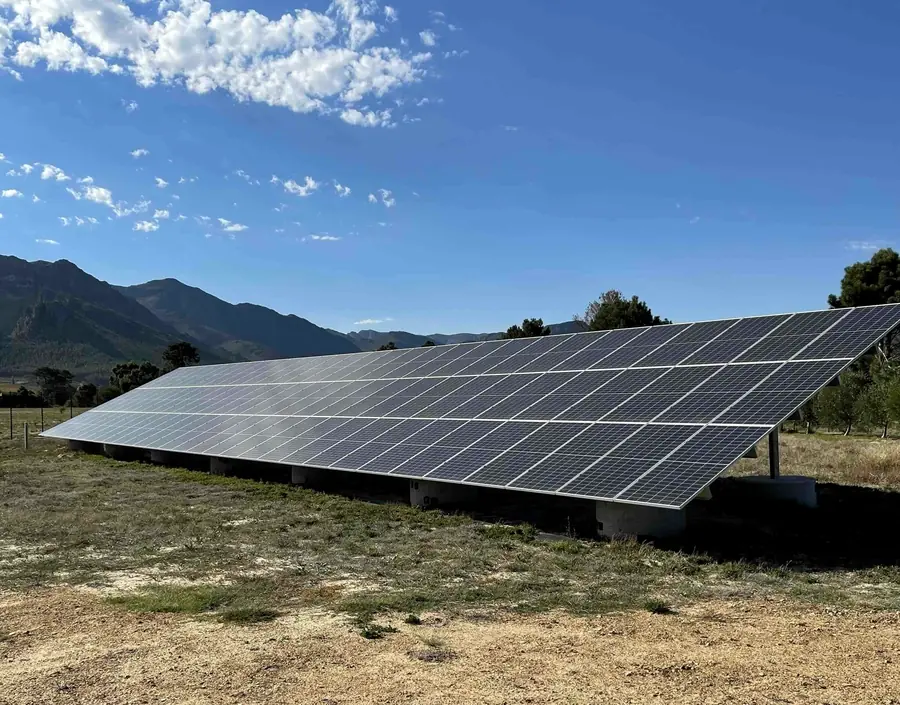 A long ground-mounted array on a farm with mountains behind
