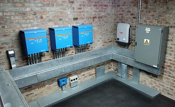 A plant room with three Victron inverters, a Fronius inverter and a DB on face brick