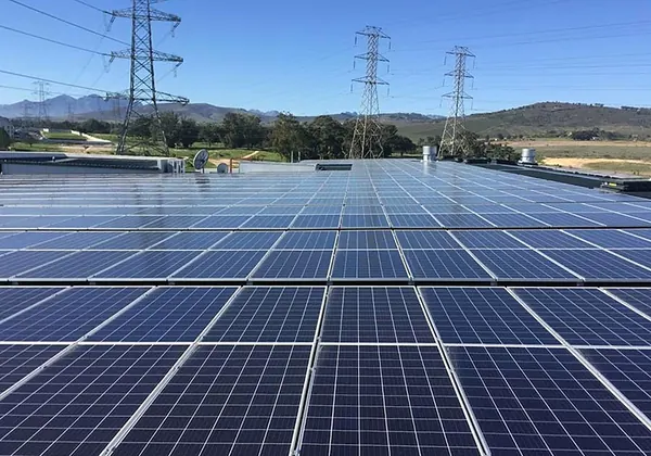 A large industrial roof array with transmission pylons behind